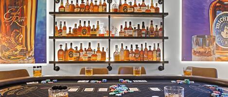 Une table de jeu de casino avec des jetons de poker et des cartes, entourée d’étagères remplies de différentes bouteilles d’alcool.