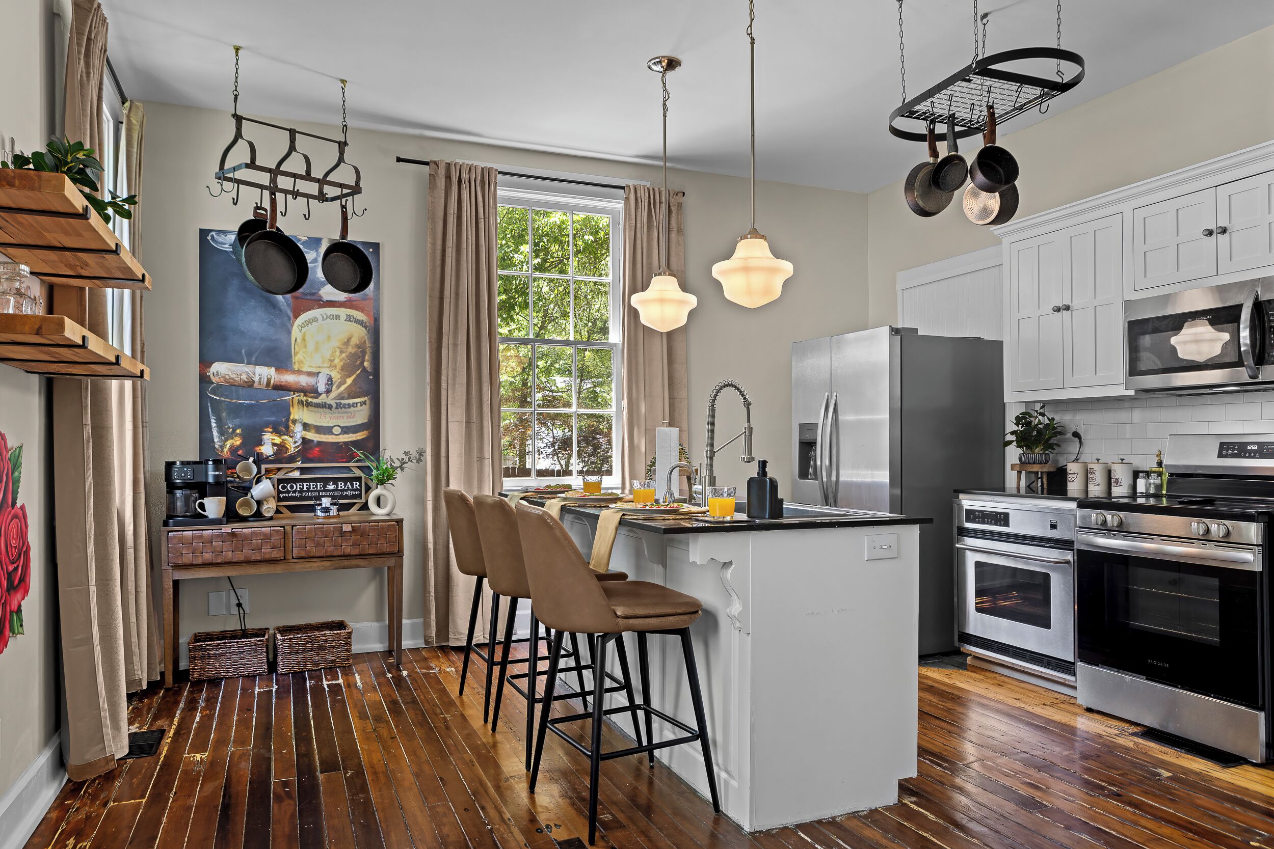 A kitchen with a central island, stainless steel appliances, hanging pots, and a coffee bar.