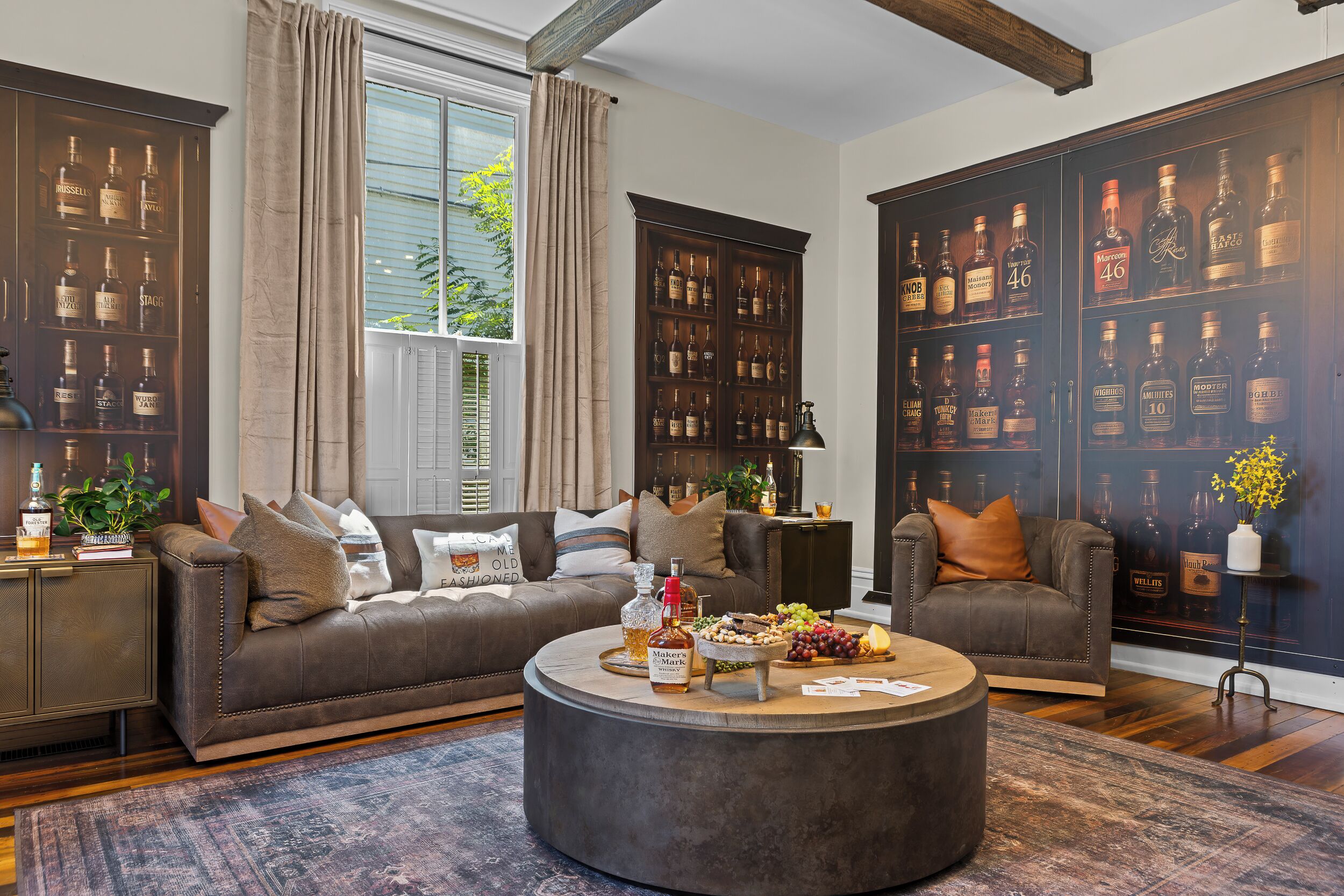 A living room with a brown leather sofa, a round coffee table with snacks, and a large liquor cabinet filled with bottles.