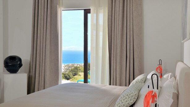 Une chambre d’hôtel avec un lit, une vue sur la mer et un vase posé sur une table de chevet.