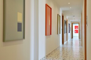 Un couloir aux murs ornés de tableaux encadrés, avec un sol à motifs et une porte au fond.