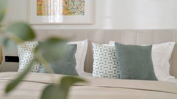 A neatly made bed with a patterned pillow and a plain pillow, a headboard, and a wall with a framed abstract painting.