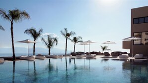 Un espace piscine avec des chaises longues et des parasols, un ciel dégagé et une vue sur la mer.