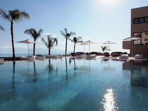A pool area with lounge chairs and umbrellas, a clear sky, and a view of the sea. - Althea Resort & Spa (Xylokastro-Evrostina)