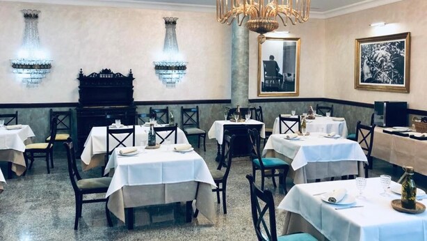 A restaurant interior with multiple tables, chairs, a chandelier, and wall-mounted decorative elements. - La Morona Hotel (Moron de la Frontera)