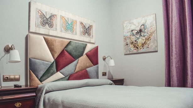 Habitación de hotel con cabecera de diseño geométrico, cama con manta texturizada, mesita de noche con lámpara y obras de arte en las paredes.