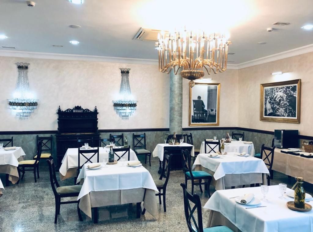A restaurant interior with multiple tables, chairs, a chandelier, and wall-mounted decorative elements.