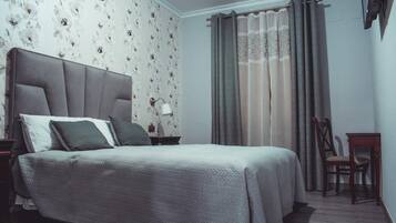 Un dormitorio con cama, mesitas de noche, una silla y una ventana con cortinas.