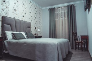 Un dormitorio con cama, mesitas de noche, una silla y una ventana con cortinas.