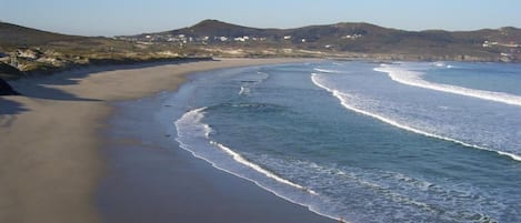 A coastal landscape with a sandy beach, waves, and distant hills.