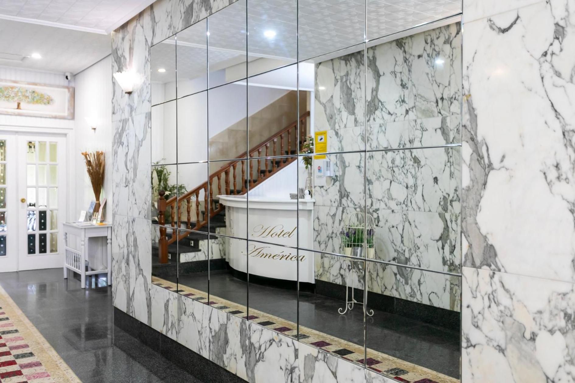 A hotel lobby with marble flooring, a reception desk, and a staircase.