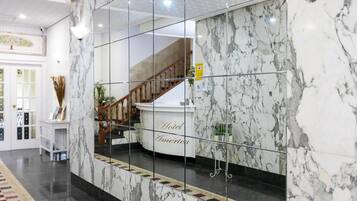 A hotel lobby with marble flooring, a reception desk, and a staircase.