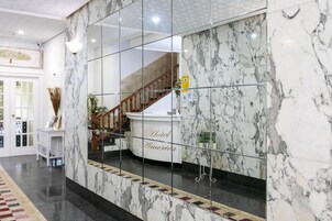 Vestíbulo de hotel con suelo de mármol, mostrador de recepción y una escalera.
