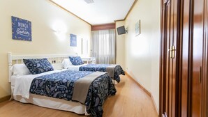 A hotel room with two beds, a wooden wardrobe, a television, and a window with curtains. - Hotel Amv Rica Ferrol (Ferrol)