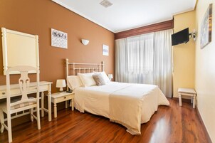 Habitación de hotel con cama, escritorio, silla, televisor y ventana con cortinas.