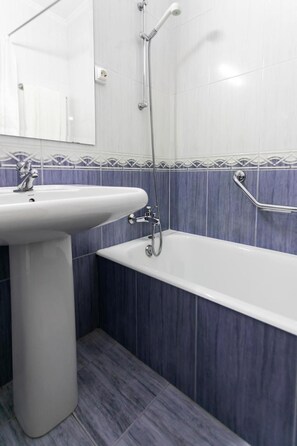 Un baño con lavamanos pedestal blanco, bañera y ducha con manguera.