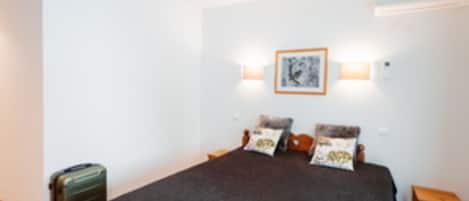 Une chambre à coucher avec un lit, des oreillers, une table de chevet, une lampe et une valise.