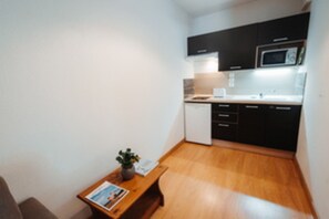 A compact kitchen with a microwave, a small refrigerator, and wooden flooring.