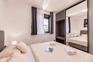 Ein Hotelzimmer mit Bett, Nachttisch mit Lampe, Spiegel und einem Fenster mit Vorhängen.