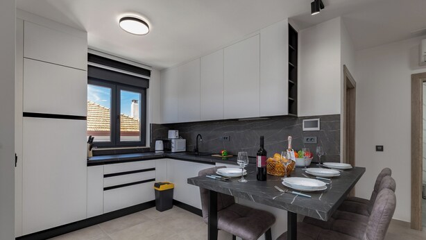 Uma cozinha moderna com armários brancos, bancada de mármore e um espaço de jantar com banquetas.