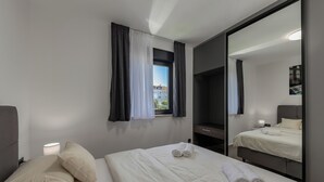 Quarto de hotel com cama, luminária, janela com cortinas, espelho e vista para prédios.