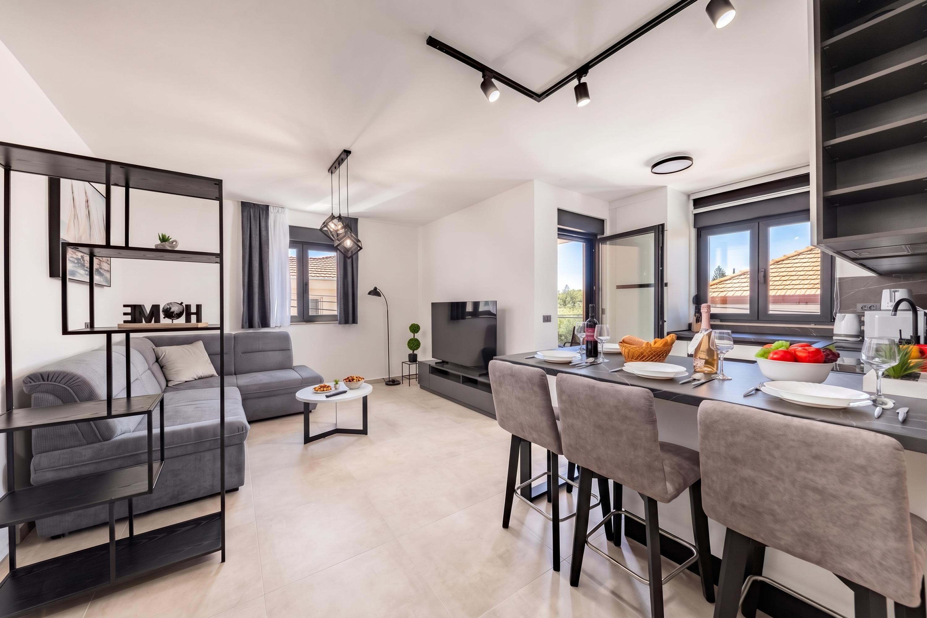 A modern kitchen with a dining area, a sofa, and a TV.