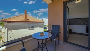 Uma varanda com mesa e cadeira, vista de um edifício com telhado de azulejos e cozinha visível por uma porta aberta.