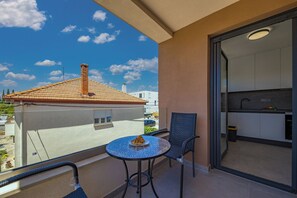 Ein Balkon mit Tisch und Stuhl, Blick auf ein Gebäude mit einem Ziegeldach und eine durch eine offene Tür sichtbare Küche.