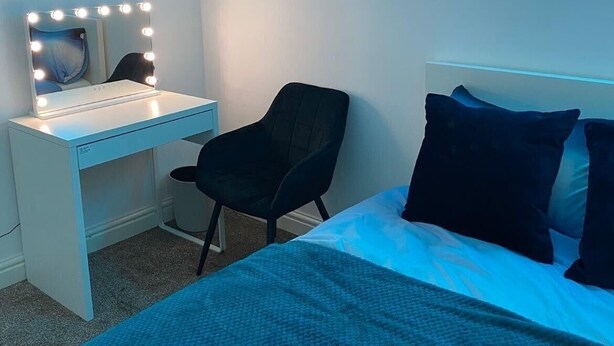 A bedroom with a bed, a desk with a mirror and lights, a chair, and a neon sign. - Inviting 1 Bed House In Bradford (Bradford)
