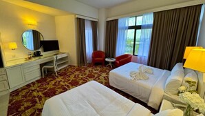 A hotel room with two beds, a desk with a chair, a TV, and a red armchair. - Royal Park Hotel (Kajang)
