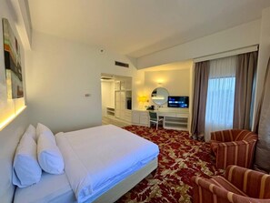 Habitación de hotel con cama, escritorio, silla, televisor y ventana con cortinas.