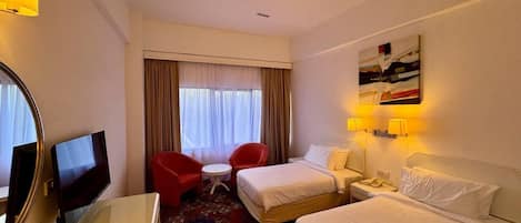 A hotel room with two beds, a desk with a flat-screen TV, a red armchair, a small round table, and a painting on the wall.