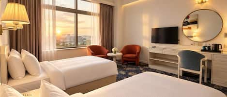 A hotel room with two beds, a desk, a TV, and a view of the city.