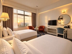 Habitación de hotel con dos camas, un escritorio, un televisor y vistas a la ciudad.