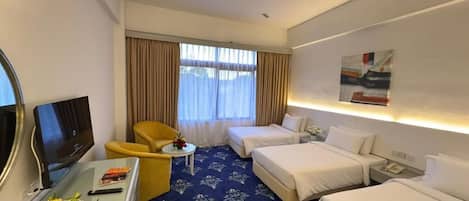 A hotel room with a bed, a desk with a TV, a chair, and a small table with a vase of flowers.
