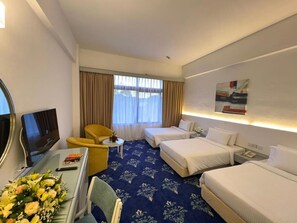 A hotel room with a bed, a desk with a TV, a chair, and a small table with a vase of flowers.