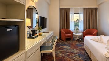 A hotel room with a bed, two chairs, a desk with a computer, a television, and a minibar.
