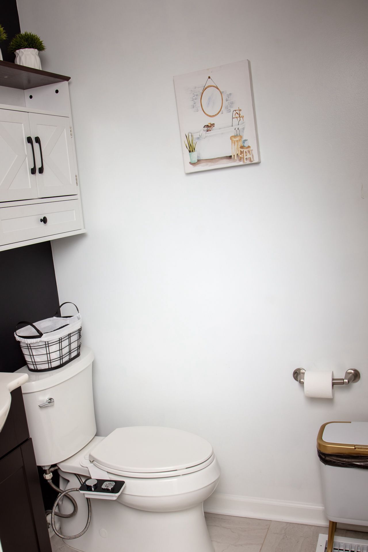 Ein modernes Badezimmer mit Toilette, Waschbecken und Schrank, alles in Weiß, wobei der Schrank schwarze Griffe hat.