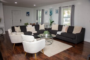 A modern living room with a dark grey sofa, white armchairs, and a glass coffee table. - Comfortable Marietta Family Home (Marietta)