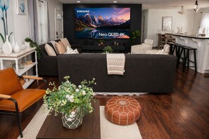 En moderne stue med et stort fladskærms-tv, en sofa, et sofabord og et spiseområde med en bar.
