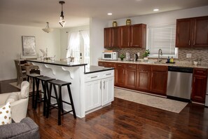 A modern kitchen with wooden cabinets, a stainless steel dishwasher, and a central island with bar stools. - Comfortable Marietta Family Home (Marietta)