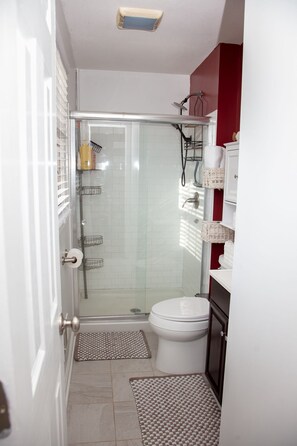 A bathroom with a glass shower enclosure, a toilet, and a sink area. - Comfortable Marietta Family Home (Marietta)