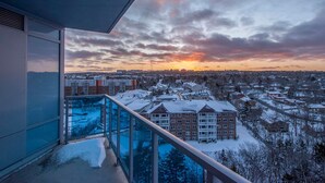 A balcony with a glass railing overlooking a snowy residential area during sunset. - Icon Bay (Halifax)