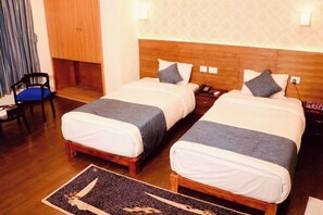 Habitación de hotel con dos camas, un cabecero de madera, un escritorio con teléfono y una silla.