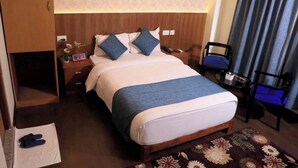 Una camera d'albergo con un letto, un comodino, una sedia, un tavolino e una sveglia a parete.