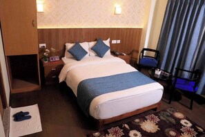 A hotel room with a bed, a nightstand, a chair, a small table, and a wall clock. - Satkar Hotel Kathmandu Pvt. Ltd (Kathmandu)