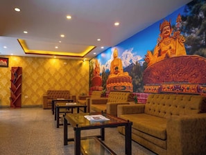 Un vestíbulo de hotel con un gran mural de Buda, zonas de estar y una recepción.