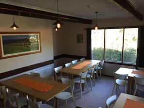 A dining area with tables and chairs, a framed picture on the wall, and a window with a view of greenery. - Winterhaus (Pambula Beach)