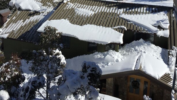 A mountain landscape with snow-covered slopes and a building with a sloped roof.