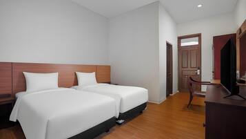 A hotel room with two beds, a wooden headboard, a desk with a chair, and a door leading to another room.